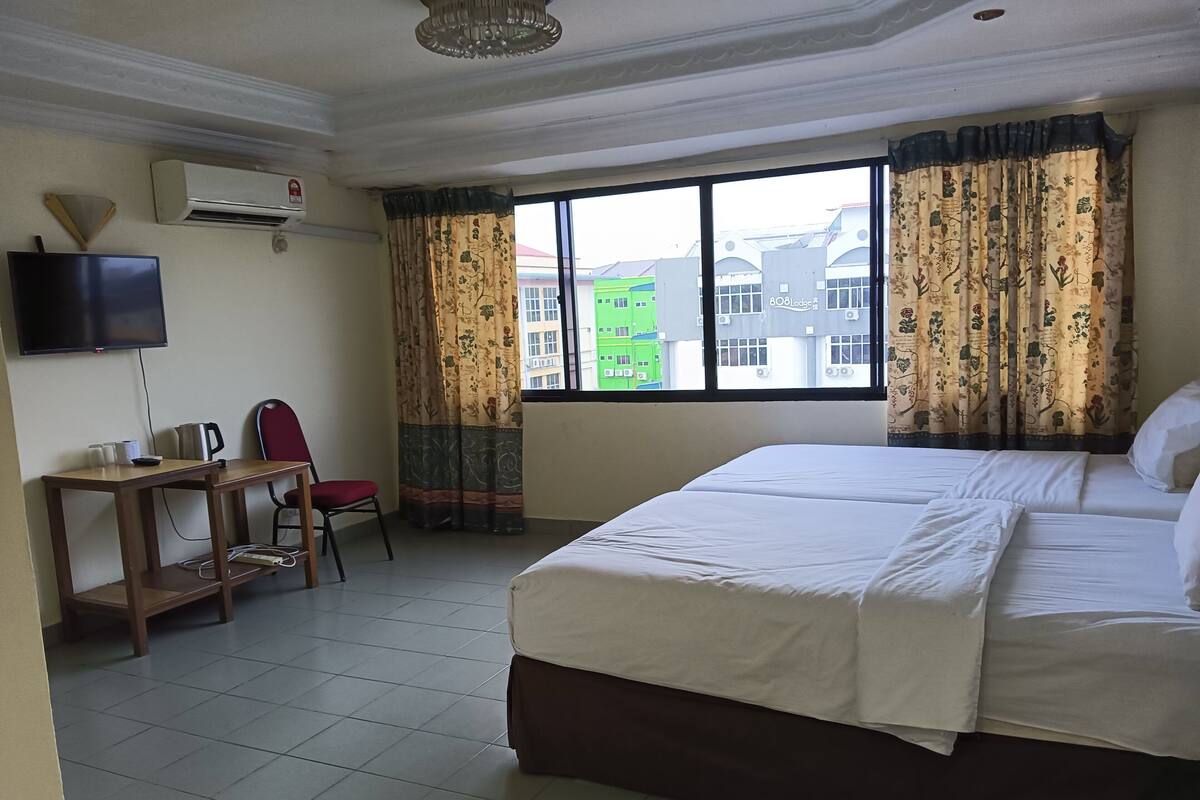 A hotel room with a large bed, a desk with a chair, a flat-screen TV, and a window with curtains.