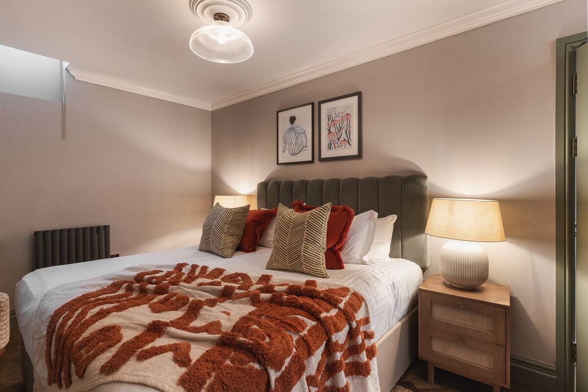 A neatly arranged bedroom with a bed, bedside tables, a lamp, and two framed pictures on the wall.