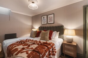 A neatly arranged bedroom with a bed, bedside tables, a lamp, and two framed pictures on the wall. - YourApartment  Cotham Arms (Bristol)