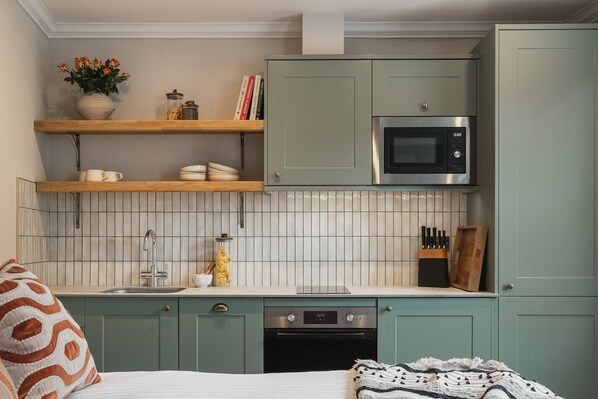 Une cuisine compacte avec des meubles de couleur turquoise, un four à micro-ondes, un lave-vaisselle et un dosseret carrelé.