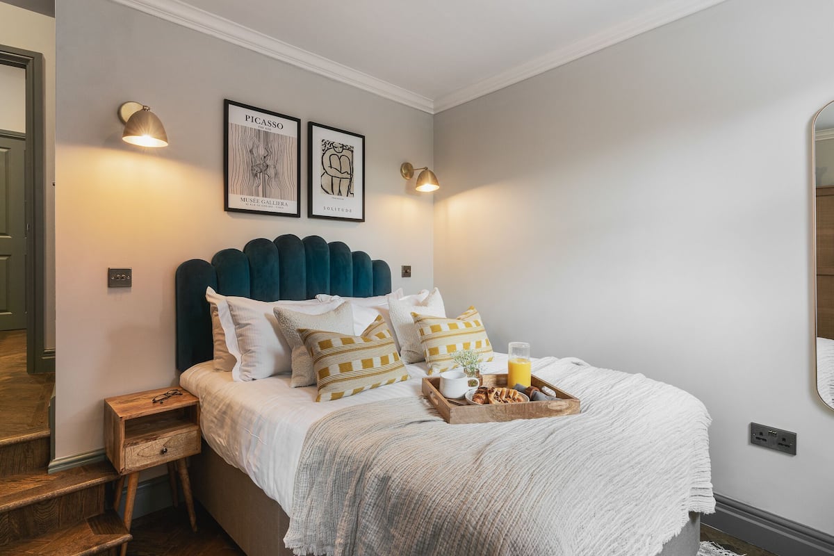 A neatly made bed with a tray of breakfast items, a bedside table with glasses, and two wall-mounted lamps.