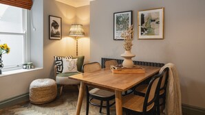 Un comedor con mesa de madera, sillas de mimbre, un reposapiés tejido y una lámpara.