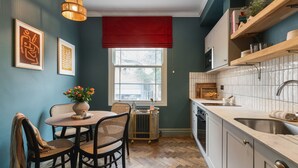 Una cocina con comedor, que cuenta con un ventanal con adornos rojos, un radiador y armarios de madera.