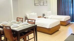A hotel room with a dining area, two beds, a nightstand, and a window with curtains. - RB Resort (Pattaya)