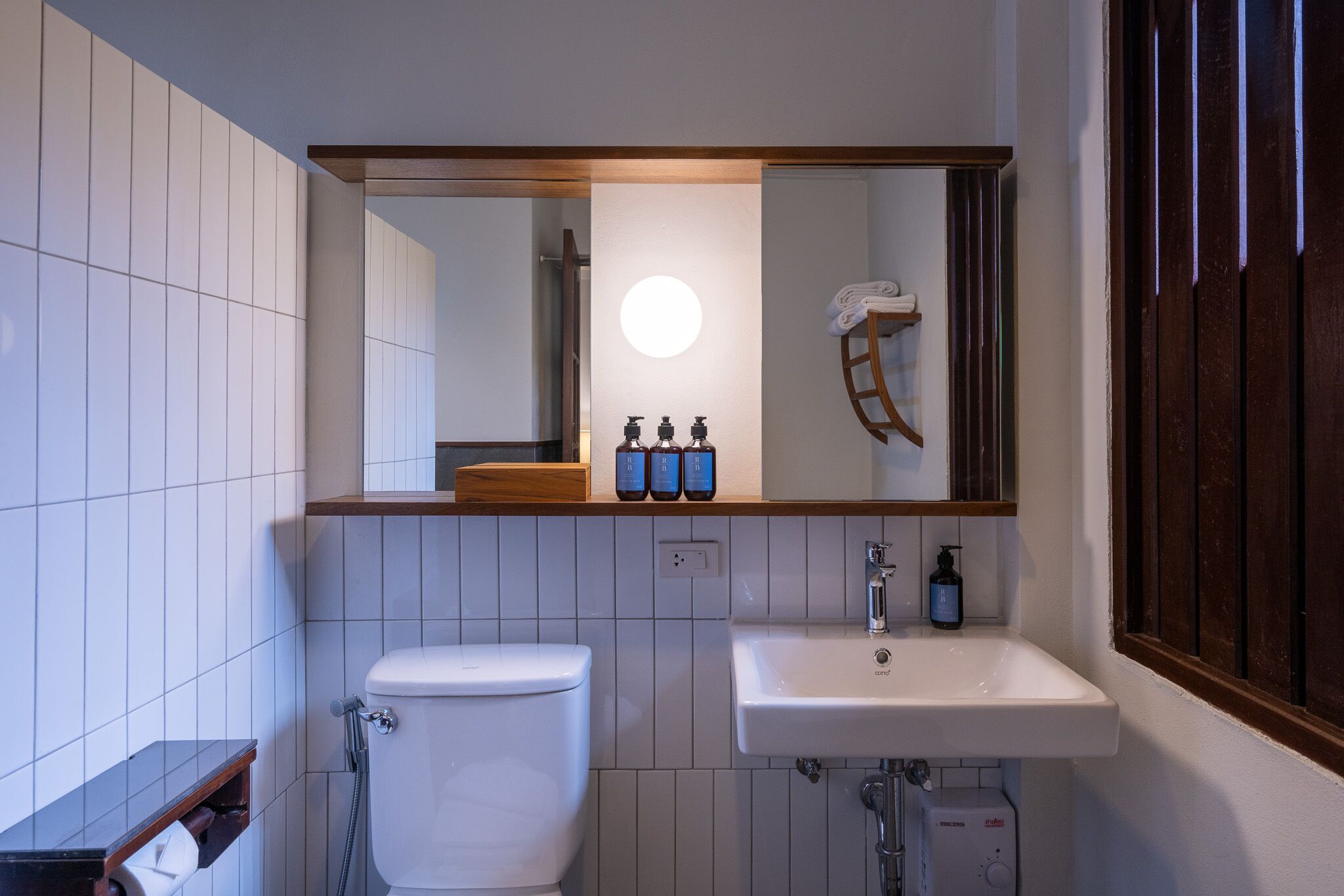A bathroom with a toilet, sink, and mirror. There are three bottles on the sink counter.