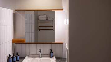 A bathroom with a sink, mirror, towel rack, and toiletries.