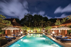 A swimming pool with lounge chairs and umbrellas, surrounded by buildings and trees. - RB Resort (Pattaya)