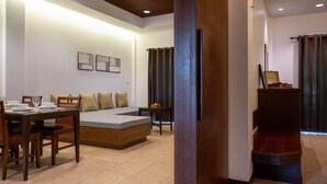 A modern hotel room with a wooden dining table set for two, a sofa bed, a small table with a lamp, and a staircase with a wooden railing. - RB Resort (Pattaya)