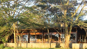 A building with a wooden structure and a concrete base, surrounded by trees and grass.