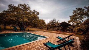 A rectangular pool with lounge chairs, surrounded by trees and a brick patio. - Kumbukgaha Villa (Sigiriya)