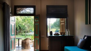 A room with a bed, a desk with a mirror, a window with a view of greenery, and a door leading outside. - Kumbukgaha Villa (Sigiriya)