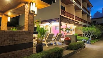 Hotel com área de estar coberta ao ar livre, parede de tijolos e entrada bem iluminada.