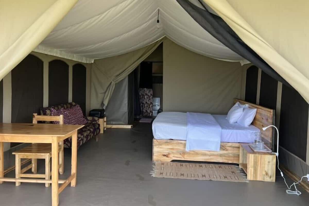 A tented accommodation with a bed, a table, and a sofa.
