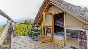 A thatched-roof tent with a wooden deck, a bed, and a chair.