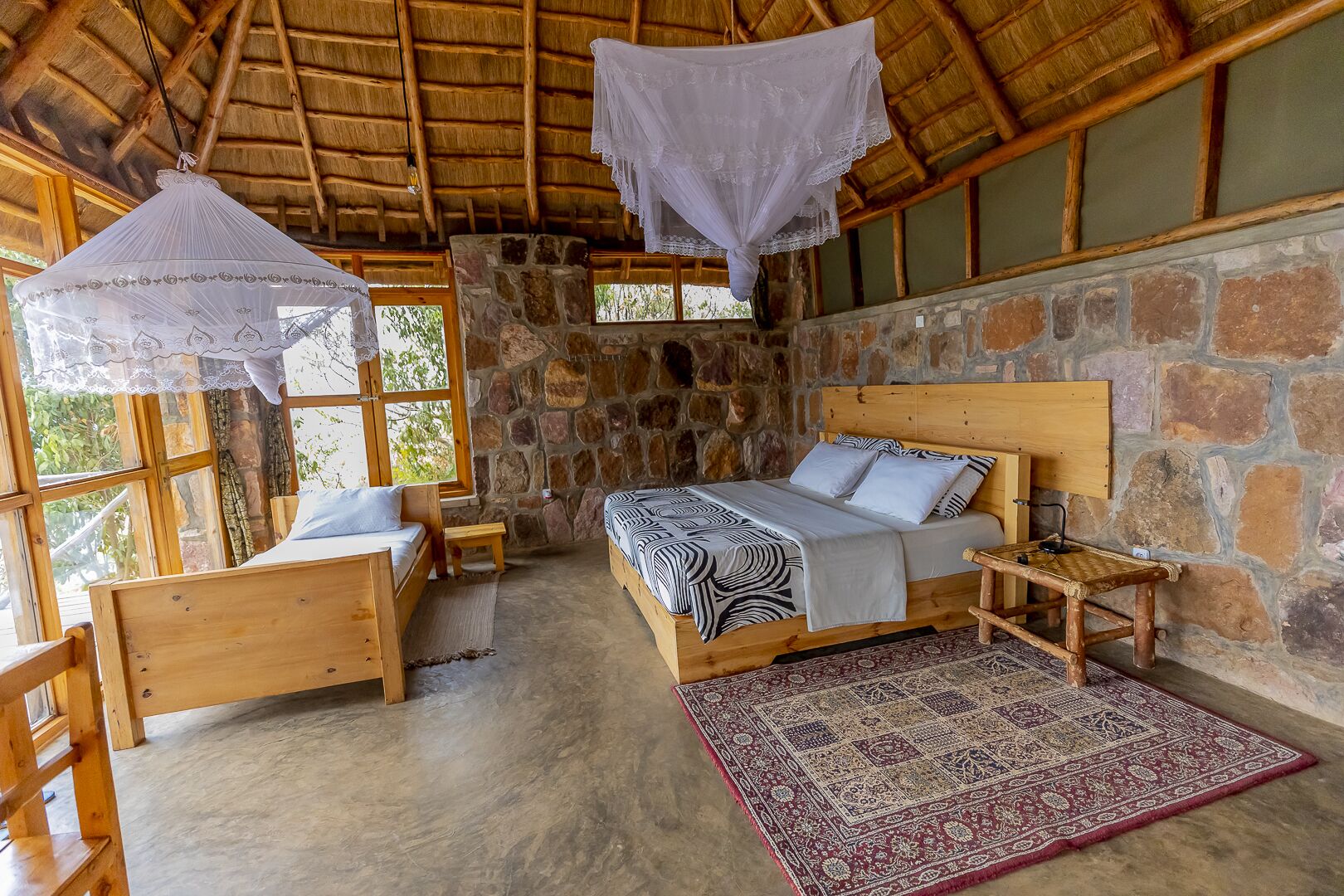 A rustic room with a stone wall, wooden furniture, a bed with patterned bedding, and a decorative rug.
