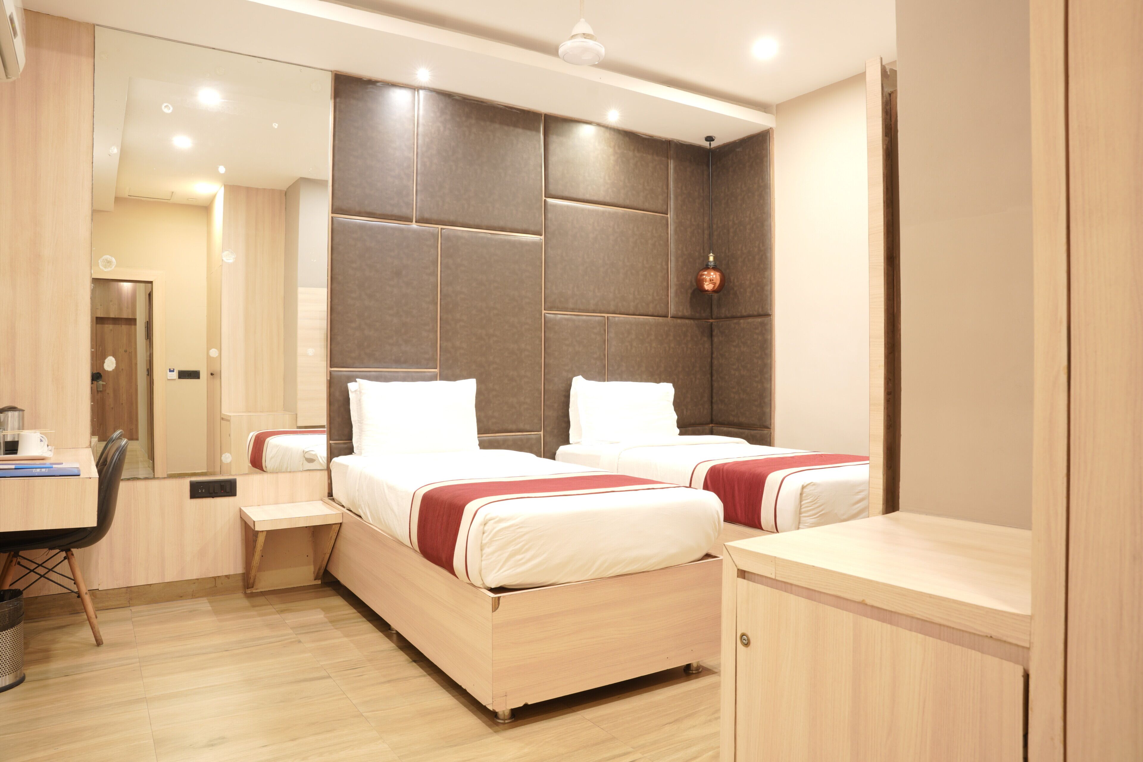 A hotel room with two beds, a desk, a chair, and a large mirror.