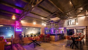 A modern bar area with exposed brick walls, neon signs, and a variety of seating options including bar stools and tables. - The Presidency Hotel In Bhubaneswar (Bhubaneshwar)