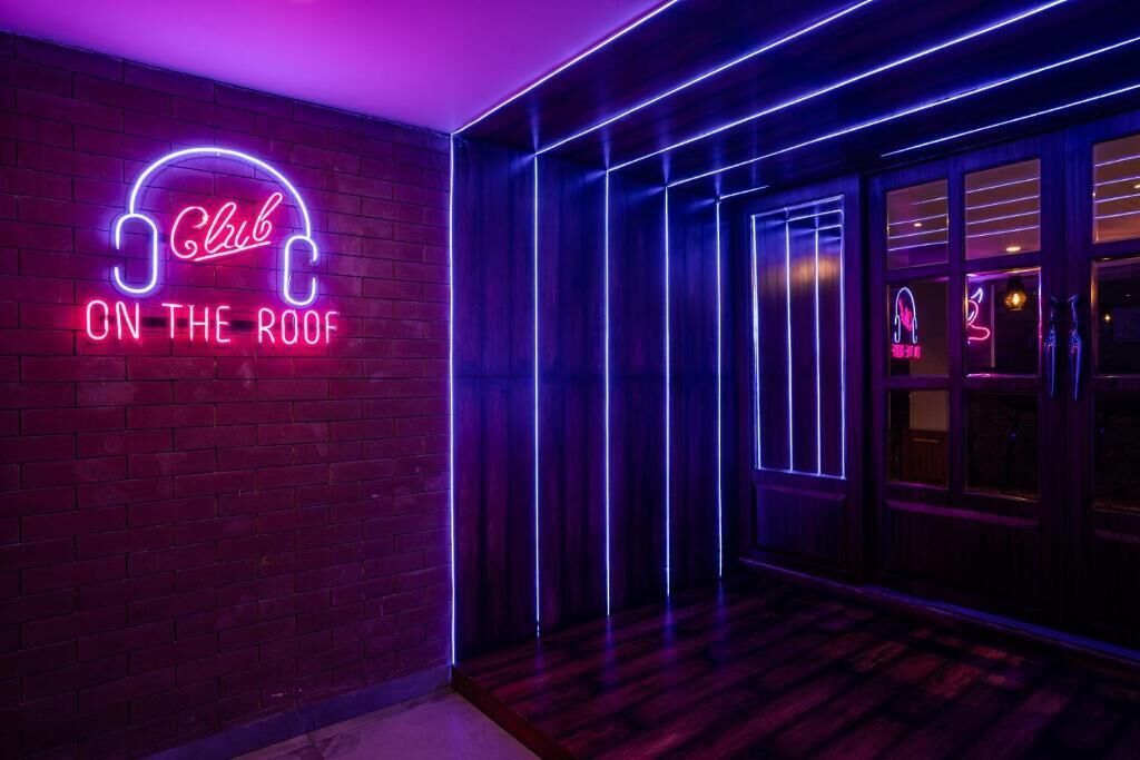 Um letreiro de neon com a inscrição 'Club On The Roof' em um corredor pouco iluminado, com piso de madeira e parede de tijolos.