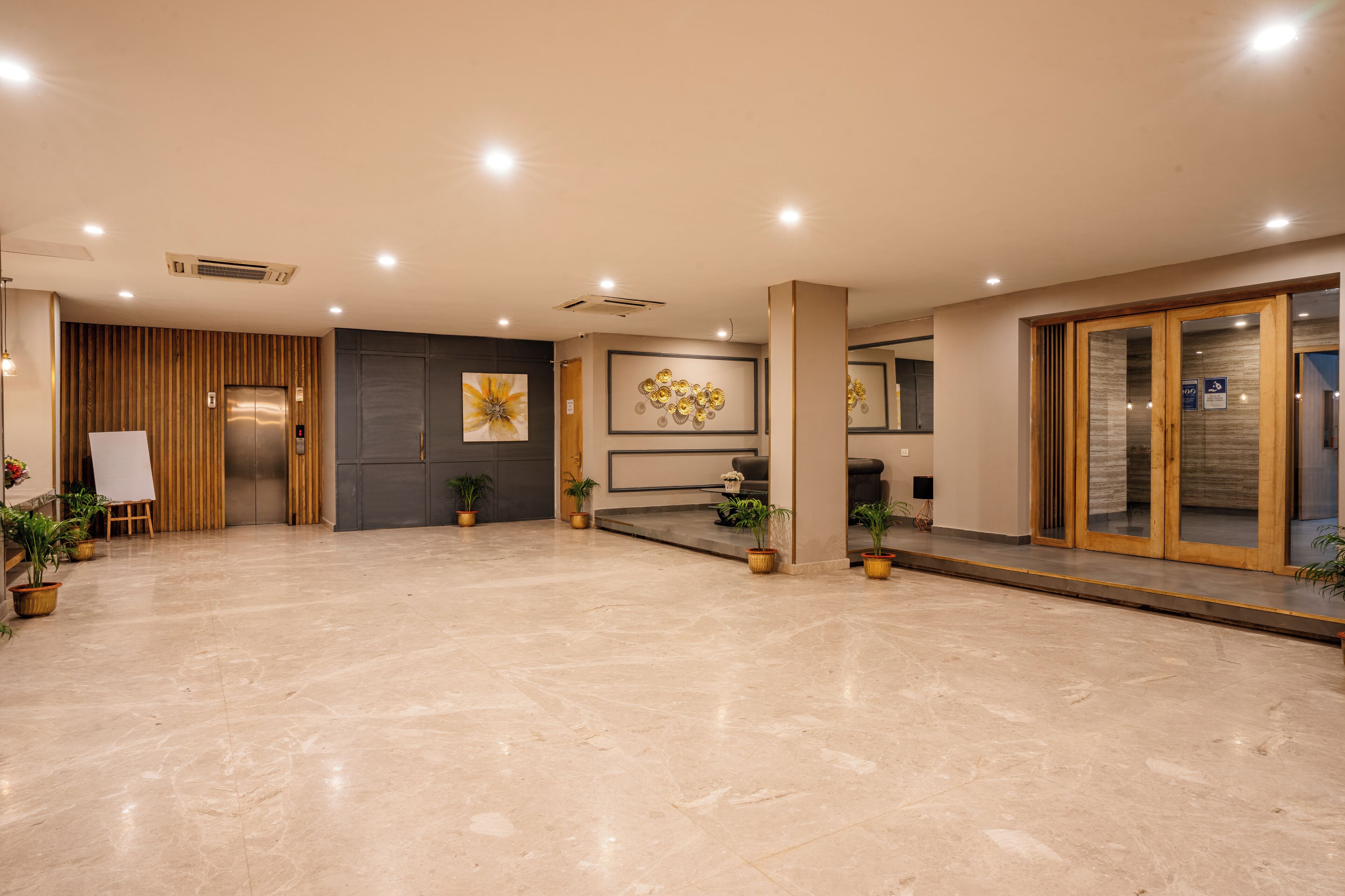 A spacious lobby with a marble floor, wooden paneling, and potted plants.