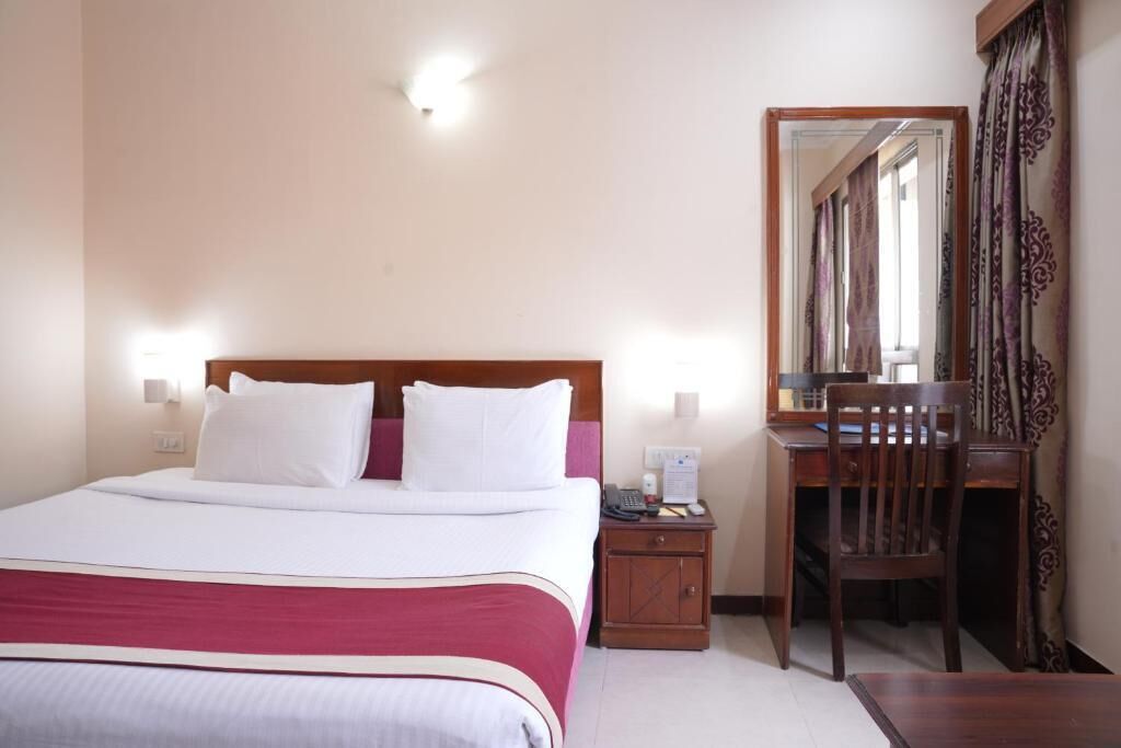 A hotel room with a bed, bedside table, desk, chair, and a mirror.