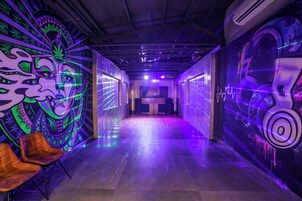 A hallway with a neon mural on the walls, a wooden floor, and a seating area with chairs.