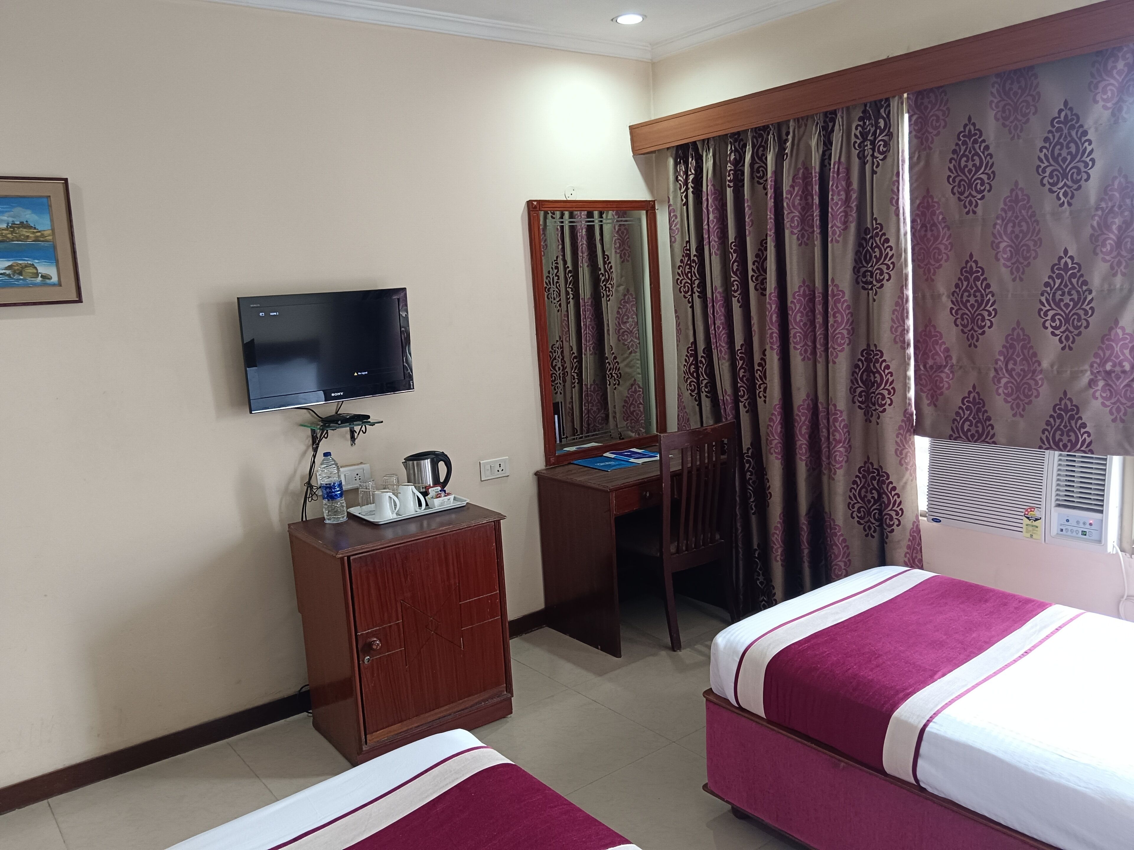 A hotel room with a bed, a desk, a television, a wardrobe, and a window with curtains.