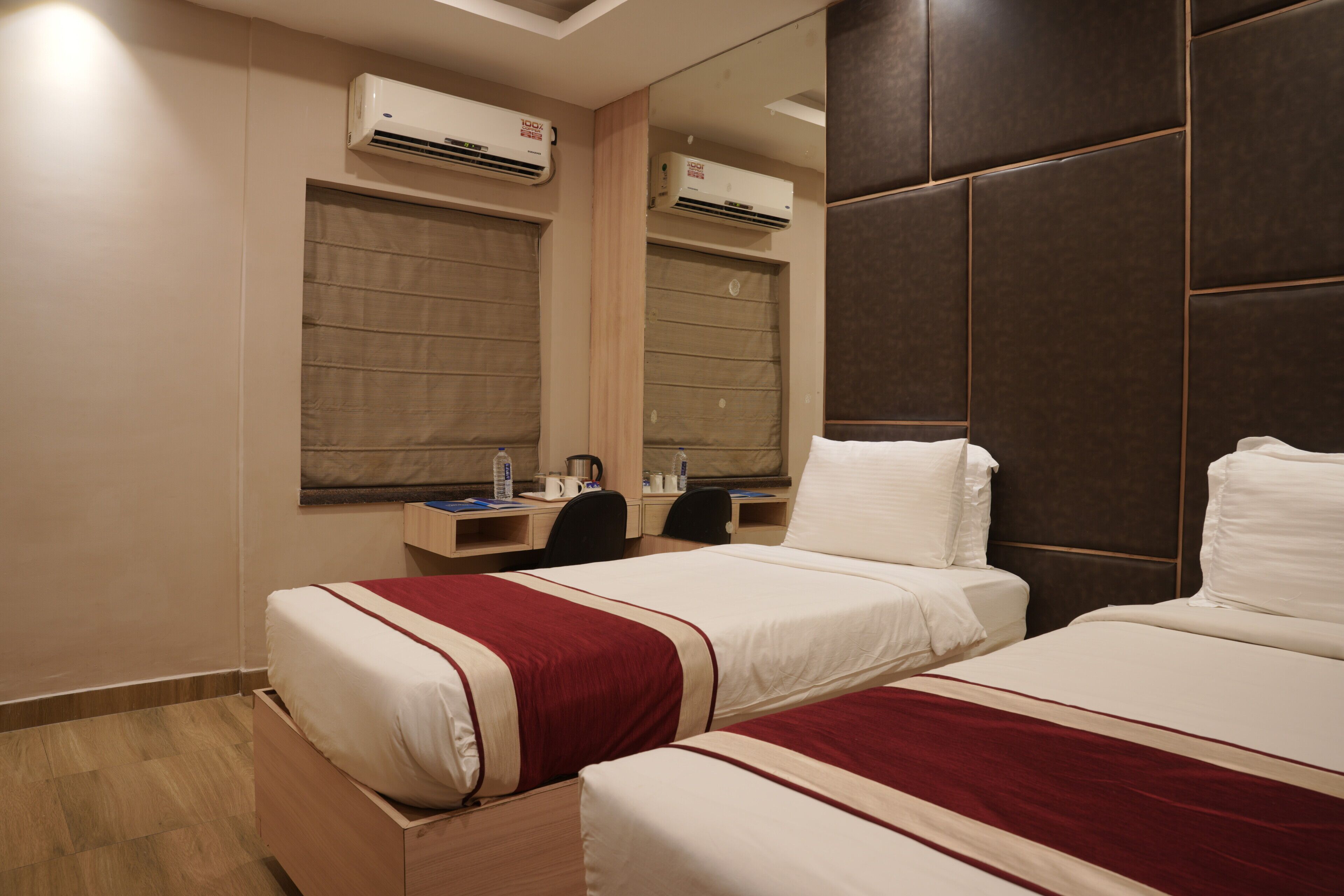 Quarto de hotel com duas camas, uma escrivaninha, cadeiras e aparelhos de ar condicionado.