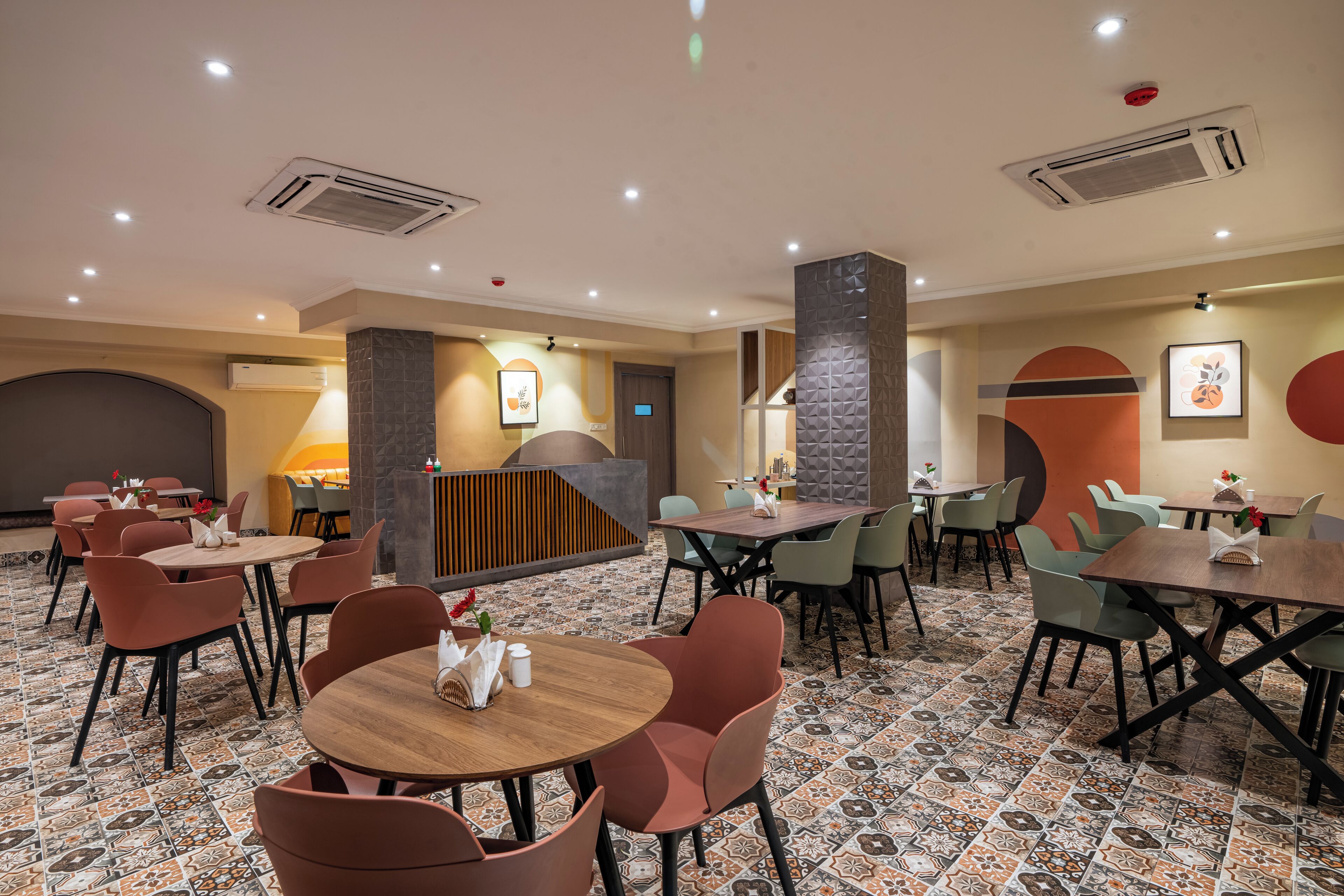 A hotel lobby with multiple dining tables and chairs, a reception area, and decorative wall art.