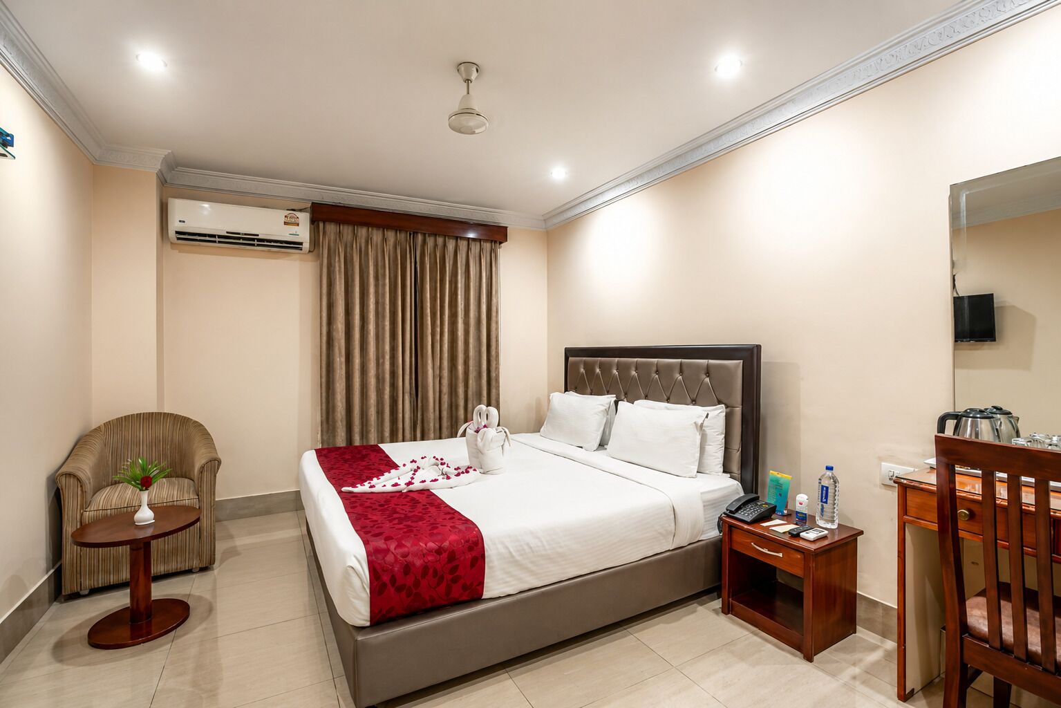 A hotel room with a bed, a chair, a desk, an air conditioning unit, and a television.