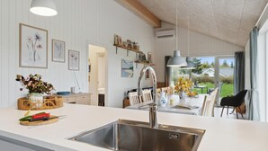 Ett modernt kök med en diskho i rostfritt stål, vita köksskåp och en matplats med utsikt över omgivningen.
