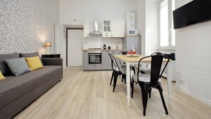 Een moderne keuken met witte kastjes, een magnetron en een fornuis. Er is een eettafel met stoelen en een bank met kussens.