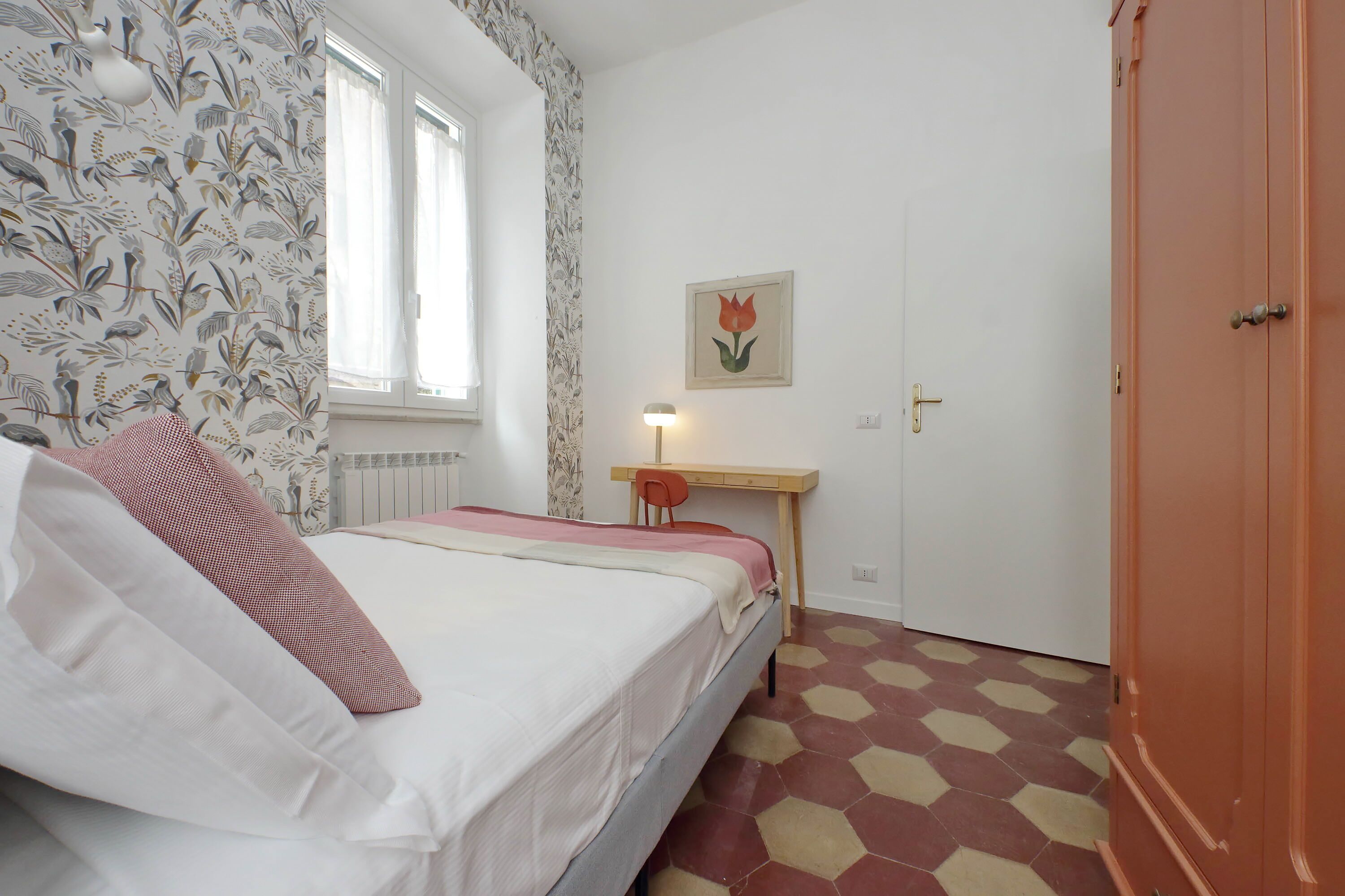 A bedroom with a bed, a desk, a chair, a door, and a window.