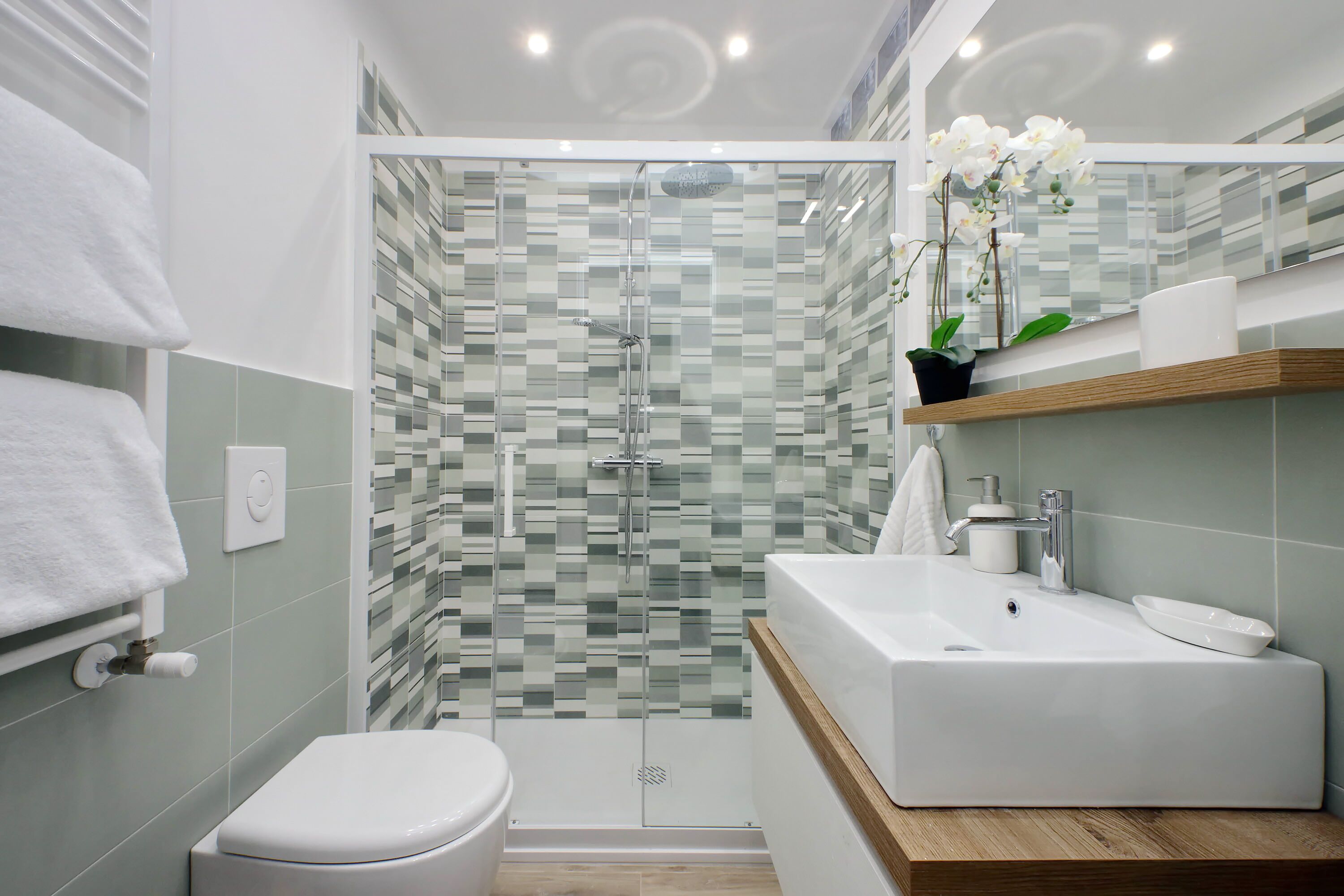 Une salle de bain moderne avec une douche à l’italienne en verre, un lavabo blanc et un meuble-vasque en bois.