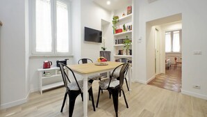 Een eetgedeelte met een houten tafel, zes stoelen, een aan de muur bevestigde televisie en een boekenkast met boeken en decoratieve objecten.