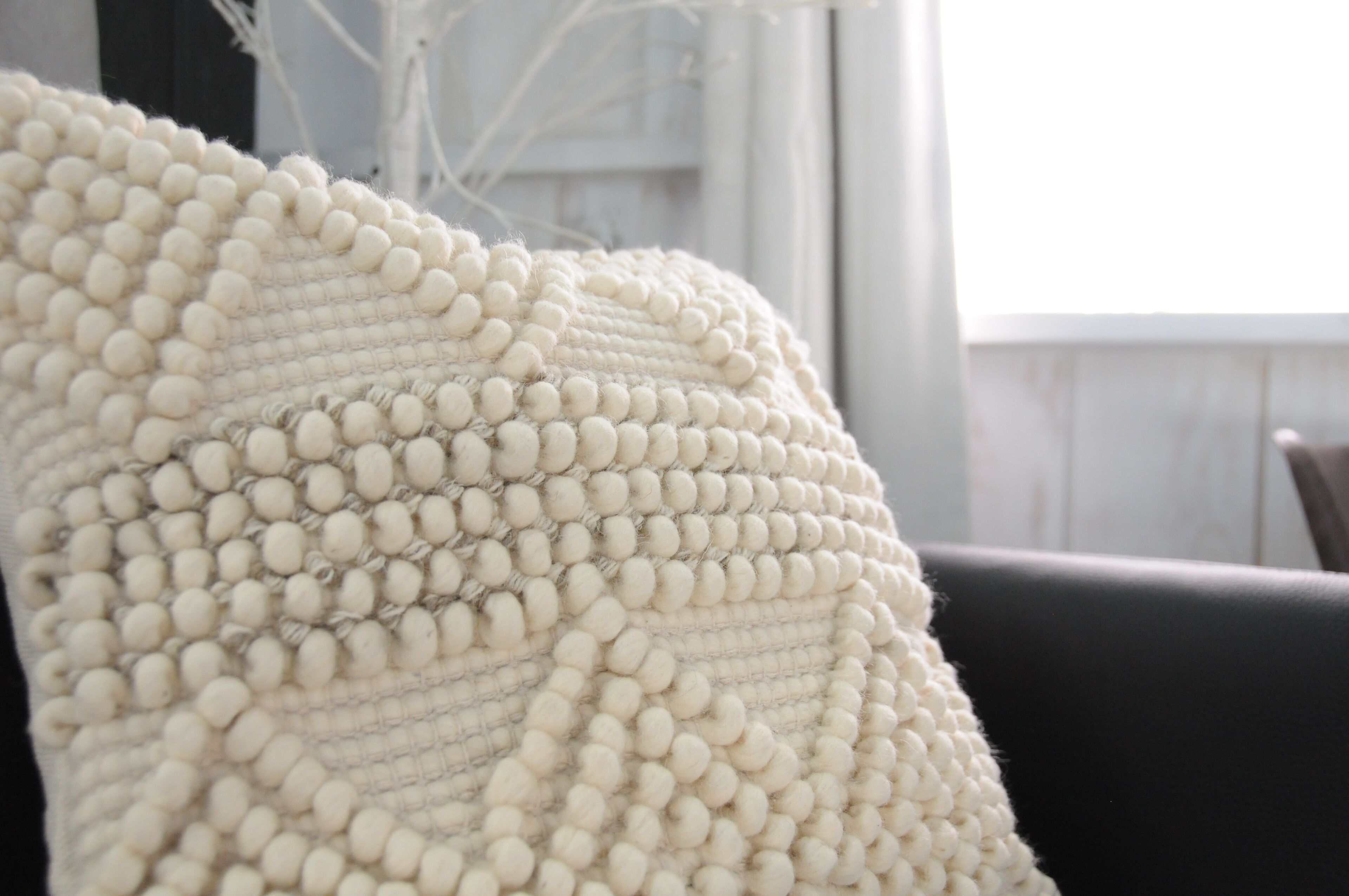 A close-up of a textured, cream-colored, knitted throw pillow with a ribbed pattern.