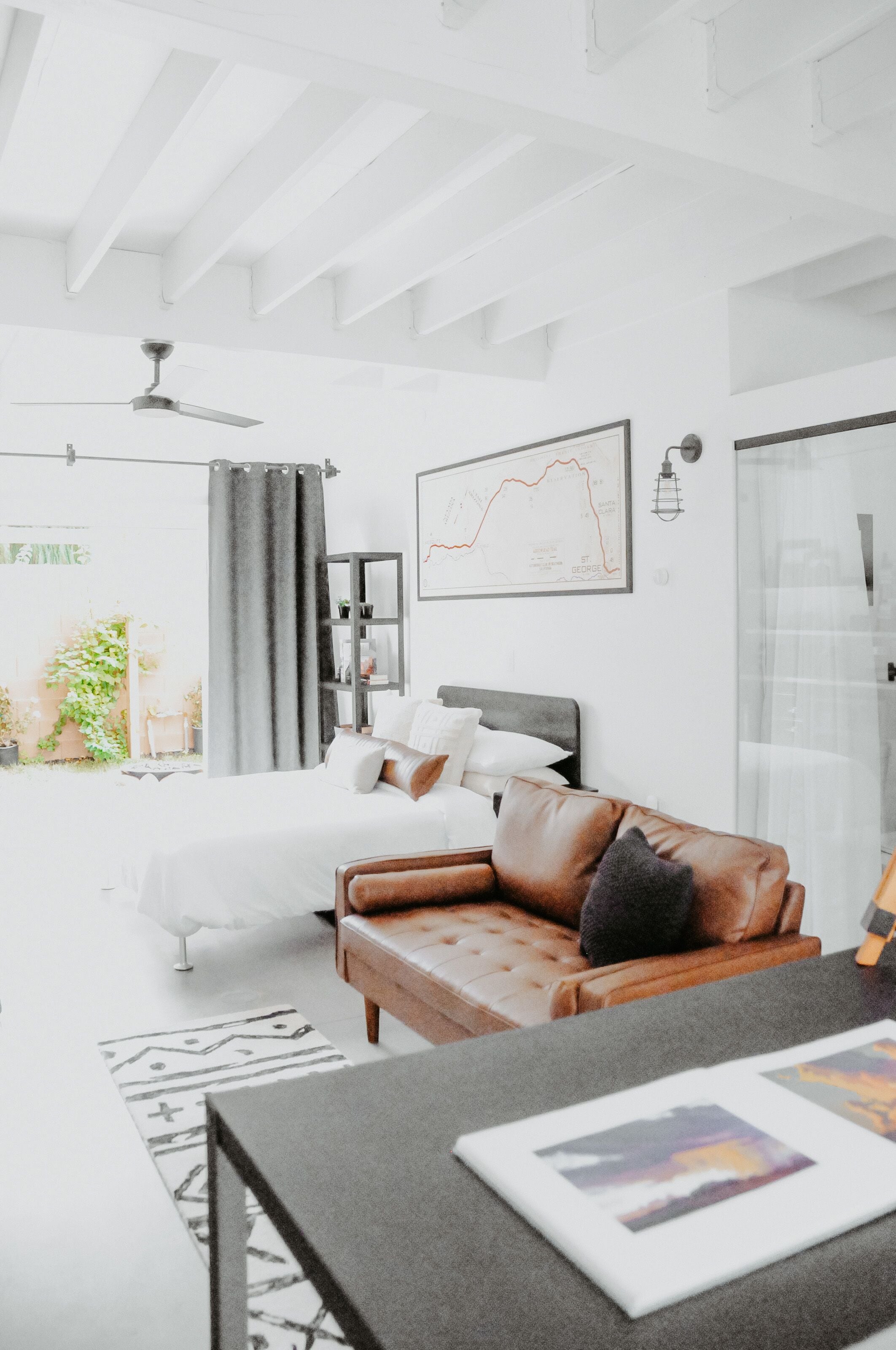 A modern bedroom with a bed, a leather sofa, a desk, and a ceiling fan.