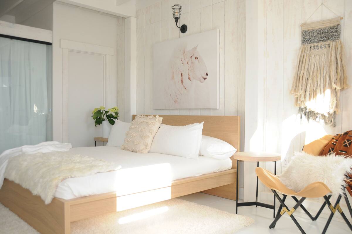 A bedroom with a bed, bedside table, chair, and a wall-mounted artwork.