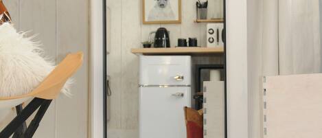 A room with a large mirror reflecting a kitchen area, a wooden chair, and a white fluffy rug.