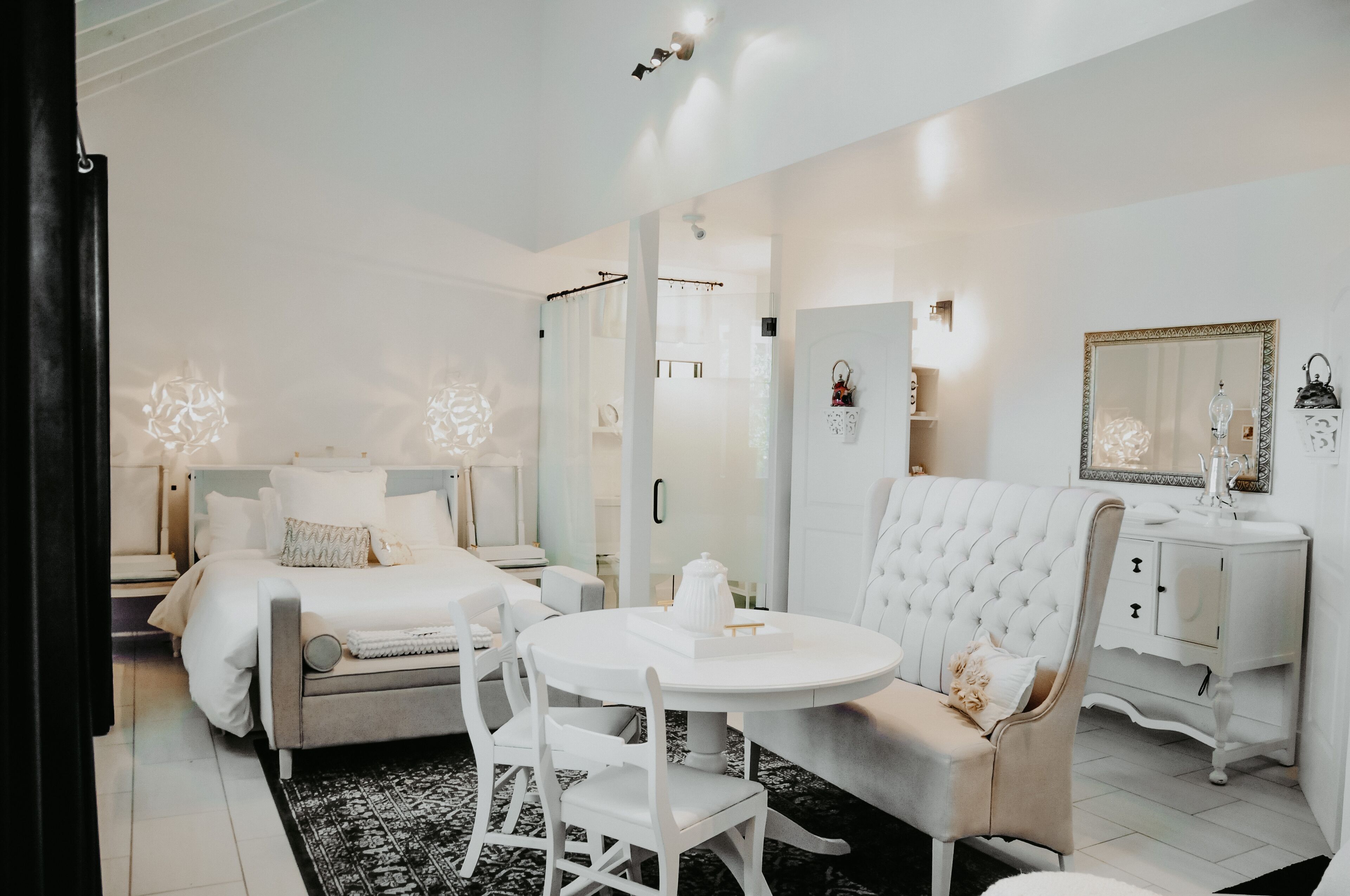 A modern, well-lit bedroom with a bed, bedside tables, a vanity, and a large mirror.