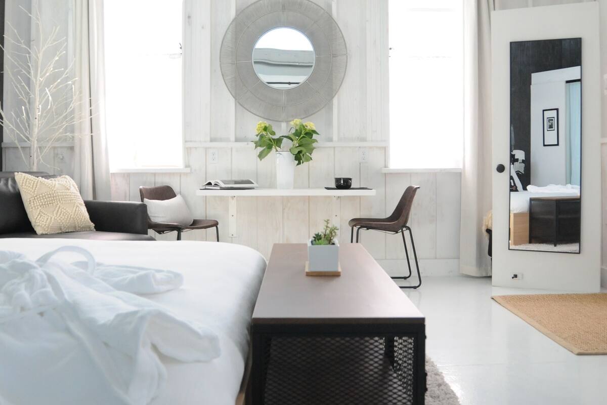 A modern bedroom with a large bed, a desk, and a mirror.