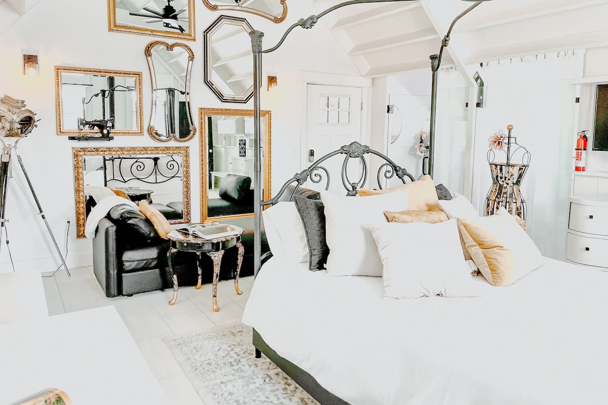 A bedroom with a large bed, multiple mirrors, and a chandelier.
