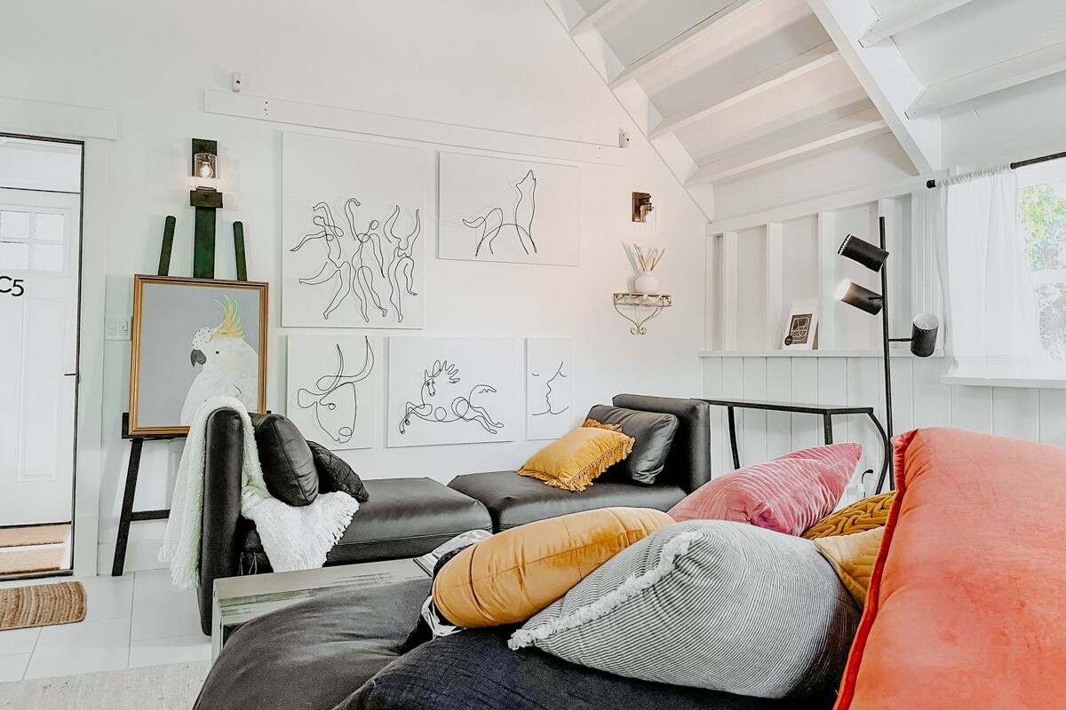 A modern living room with a black leather sofa, colorful cushions, and abstract art on the walls.
