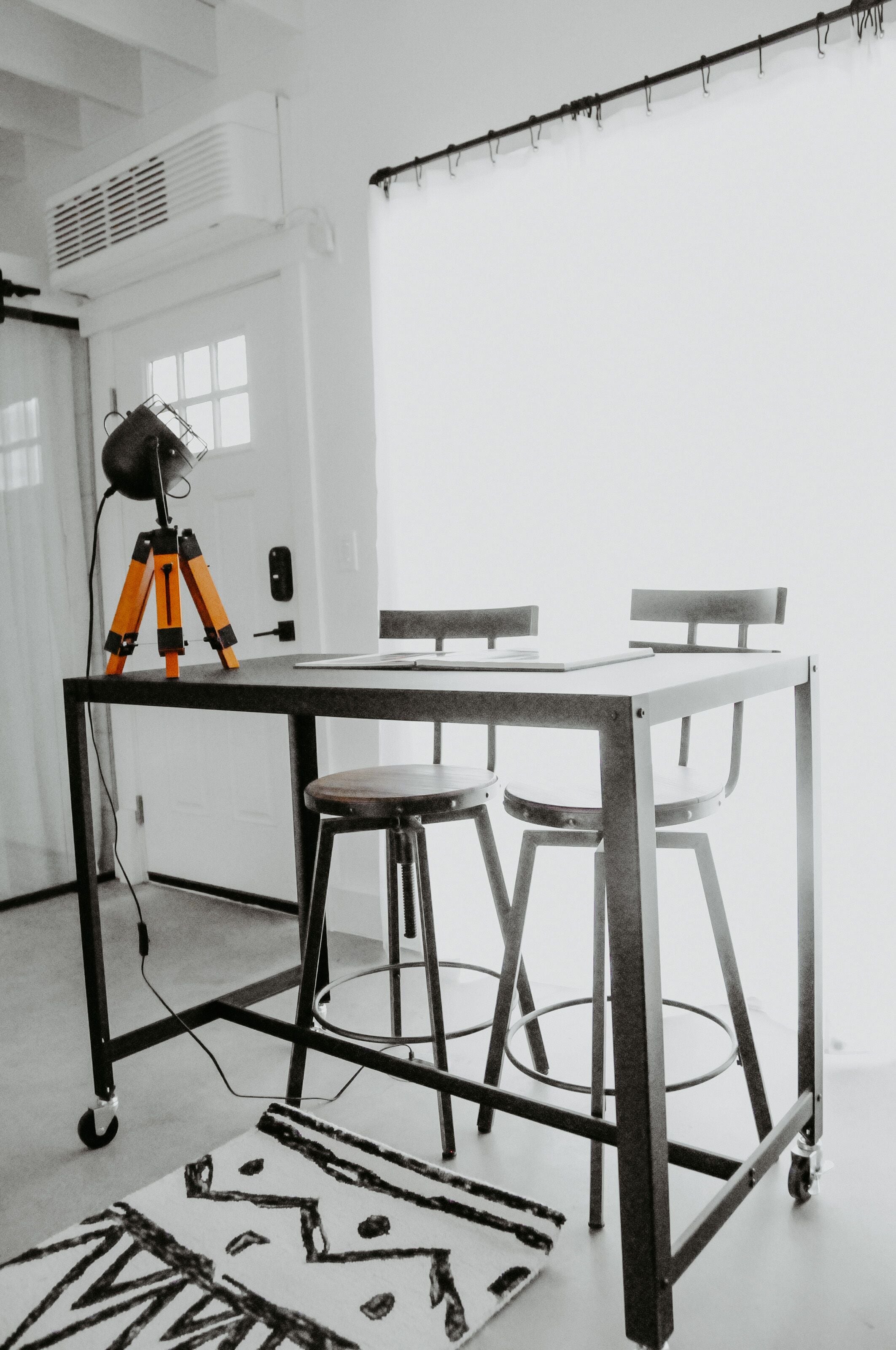 A studio with a tripod-mounted camera on a table, two chairs, and a large window.