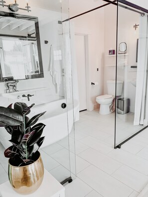 A modern bathroom with a glass shower enclosure, a white bathtub, and a large mirror above the sink.