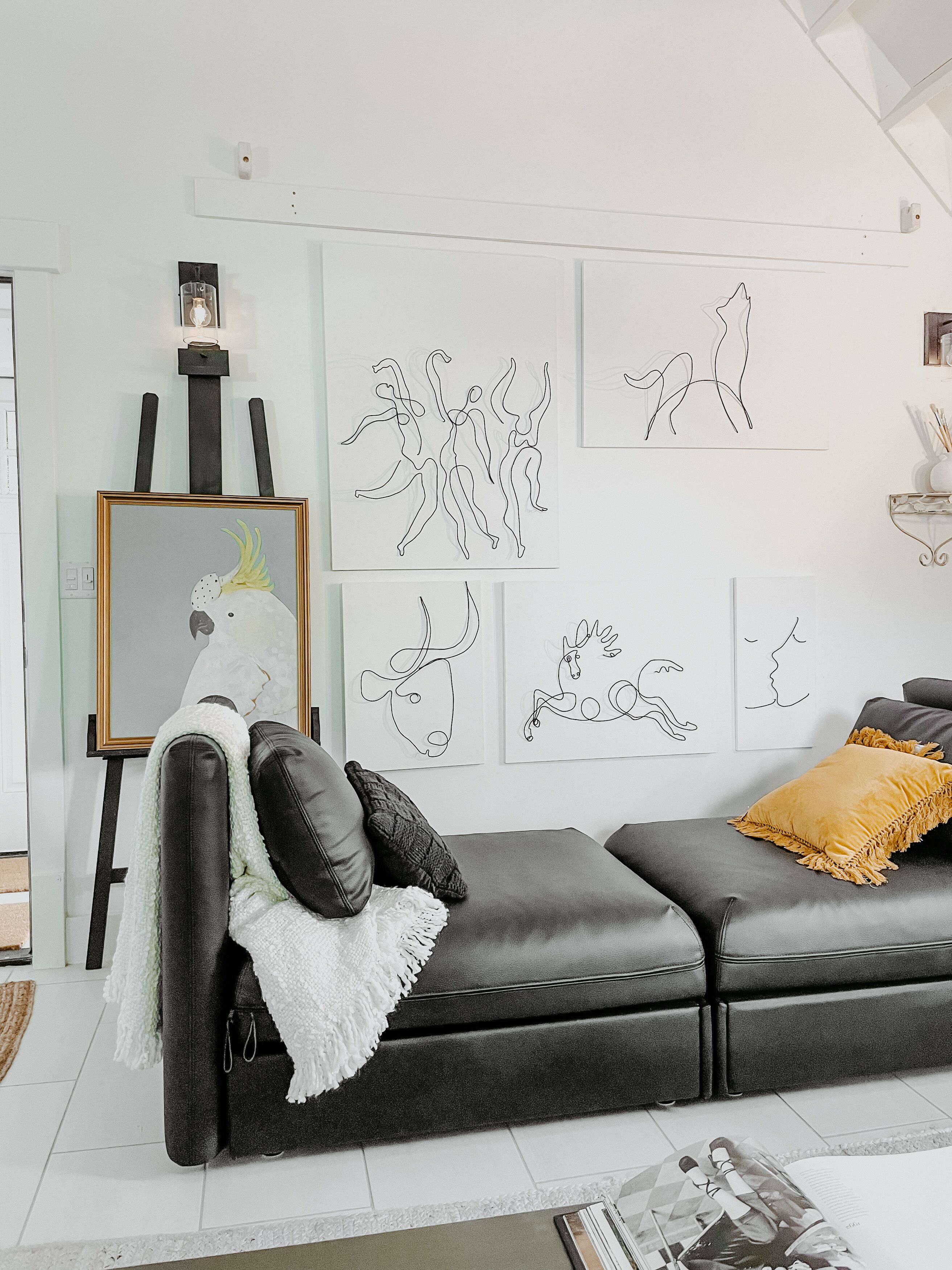 A modern living room with a black leather sofa, a white throw blanket, and a framed artwork on an easel.