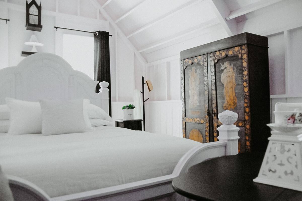 A bedroom with a large bed, a wardrobe, a nightstand, and a wall clock.