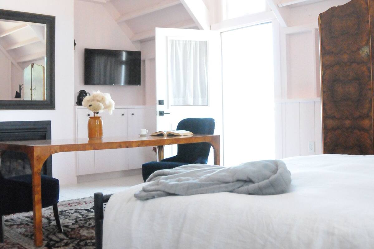 A bedroom with a large bed, a desk, a chair, a television, and a ceiling fan.