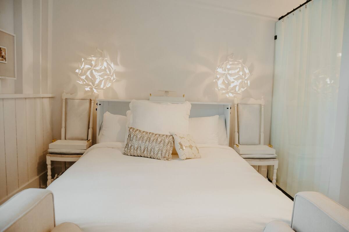 A neatly made bed with white linens and two decorative wall sconces.
