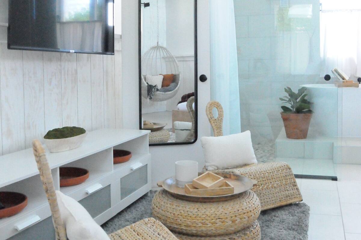 A modern living room with a large mirror, wicker furniture, and a white tiled floor.