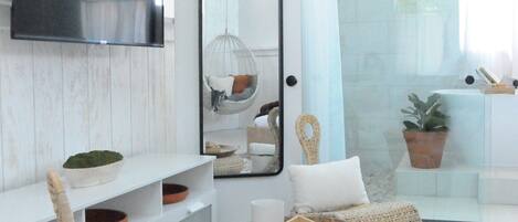 A modern living room with a large mirror, wicker furniture, and a white tiled floor.